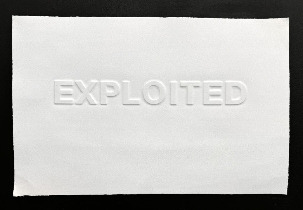 A piece of white Somerset paper with the word Exploited embossed on it in capital letters on a black background
